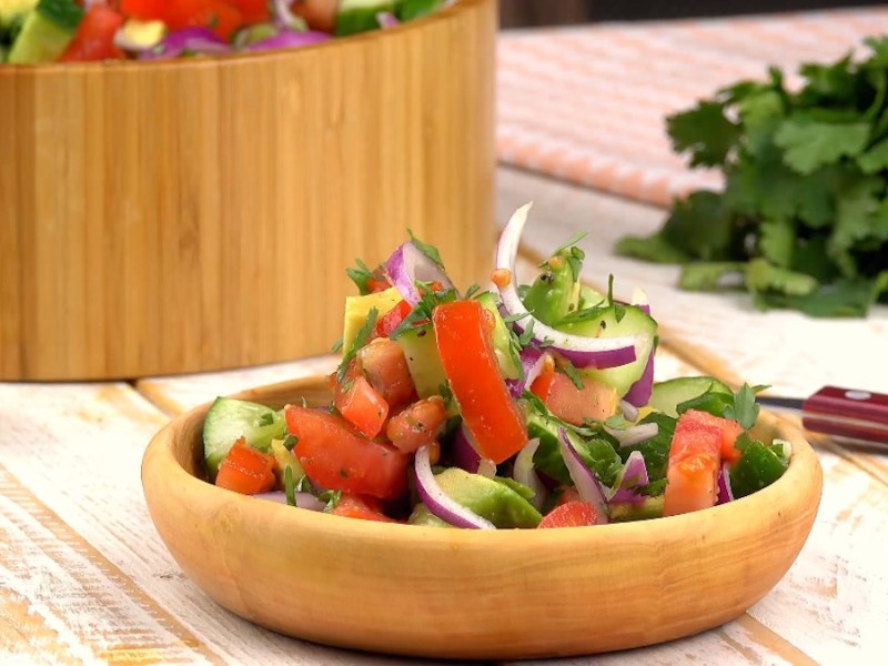 Eine Holzschale mit Guacamole-Salat. Im Hintergrund ein Bund Koriander und eine gro0e Schüssel mit Salat.