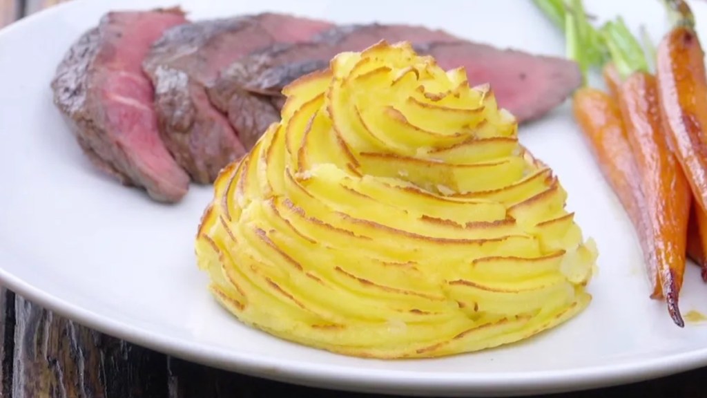 Ein Kartoffel-Turm neben Fleisch und Möhren auf einem Teller.