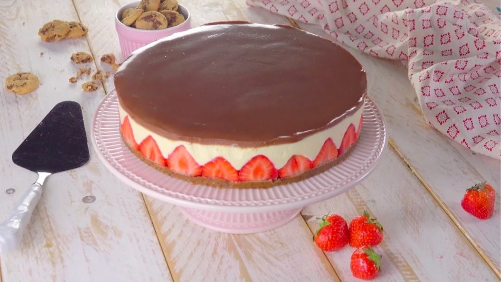 Eine Erdbeer-Torte auf einer Kuchenplatte, daneben frische Erdbeeren und ein Tortenheber.