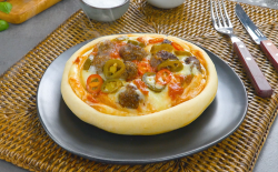 Ein Pizza Pot Pie mit Jalapeños und Chilis auf einem Teller. Daneben liegt Besteck.