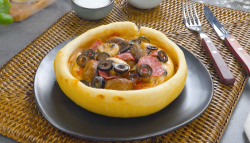 Ein Pizza Pot Pie mit Oliven und Champignons auf einem Teller. Daneben liegt Besteck.