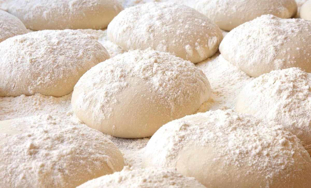 Viele rund geformte Pizzateige, die mit Mehl bestäubt sind.