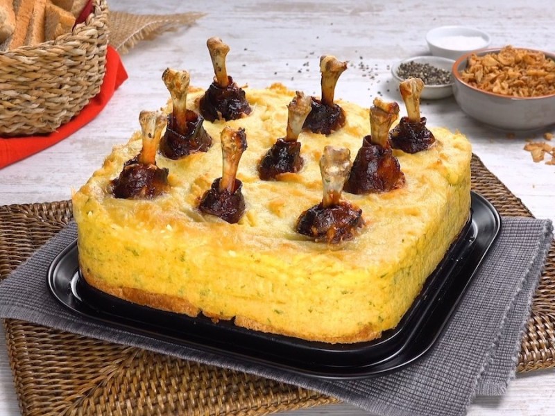 Ein Hähnchenkeulen-Kuchen, daneben ein Korb Brot, eine Schale mit Röstzwiebeln und eine mit Dip.