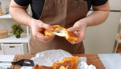 Eine gefüllte Kartoffelpizza wird von einem Koch mit den Händen auseinander gezogen. Darunter liegen weitere Pizzen auf der Arbeitsplatte.
