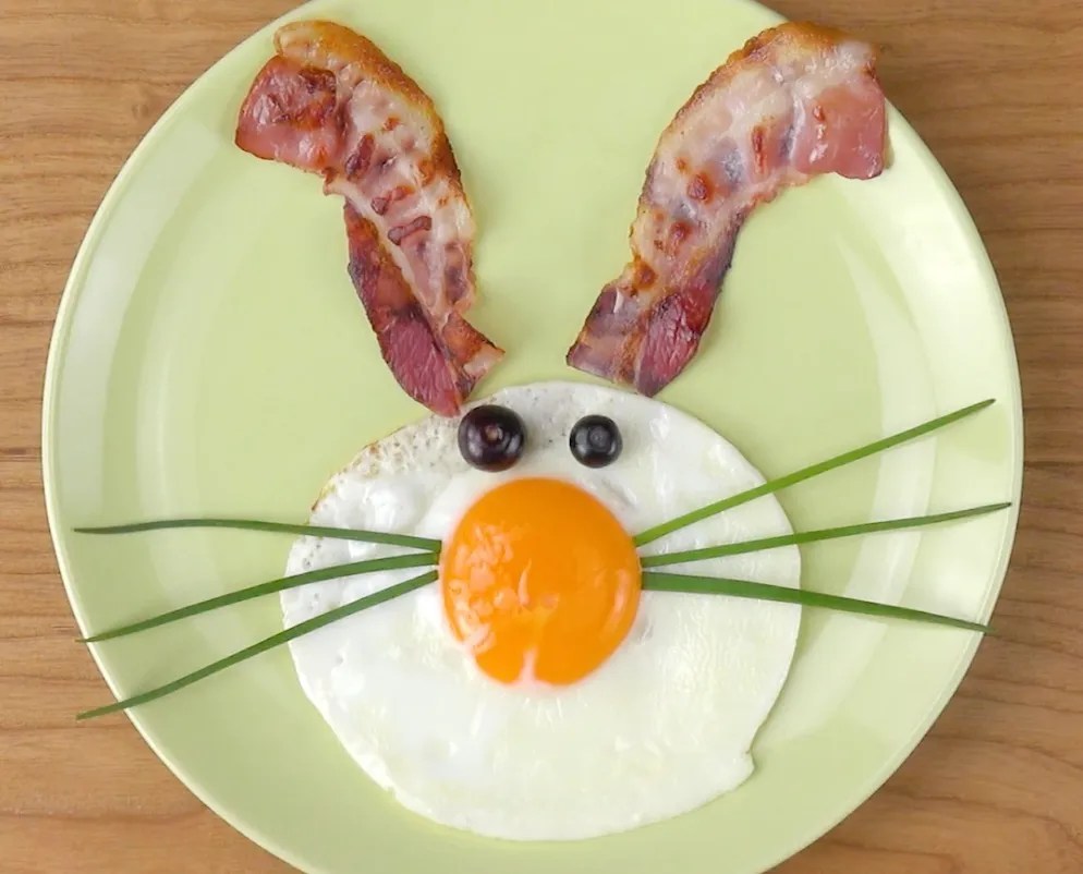 Osterfrühstück: Ein Hasengesicht mit Bacon und Ei auf einem grünen Teller.