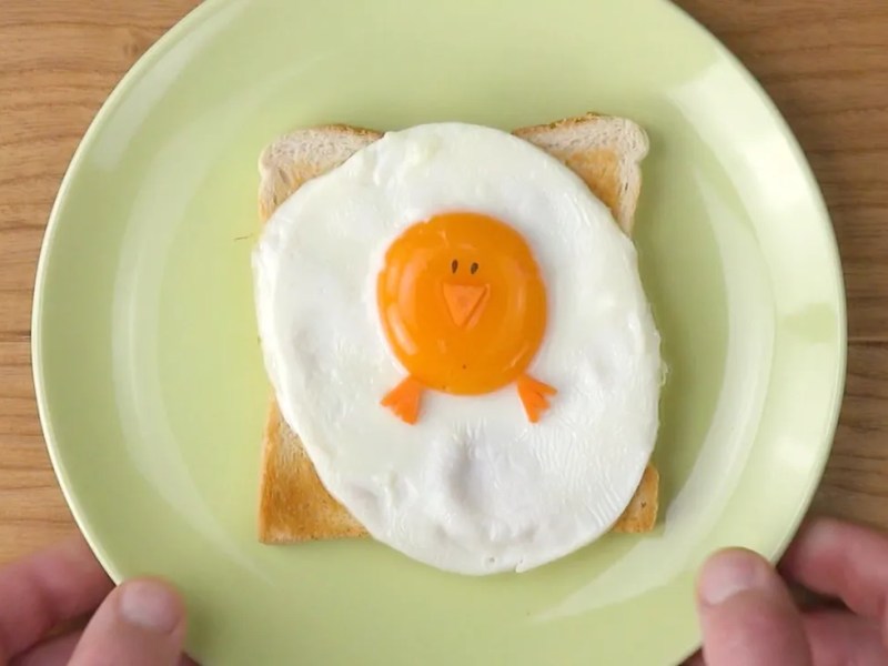 Osterfrühstück: Ein Küken aus Ei auf einem Toast auf einem grünen Teller.