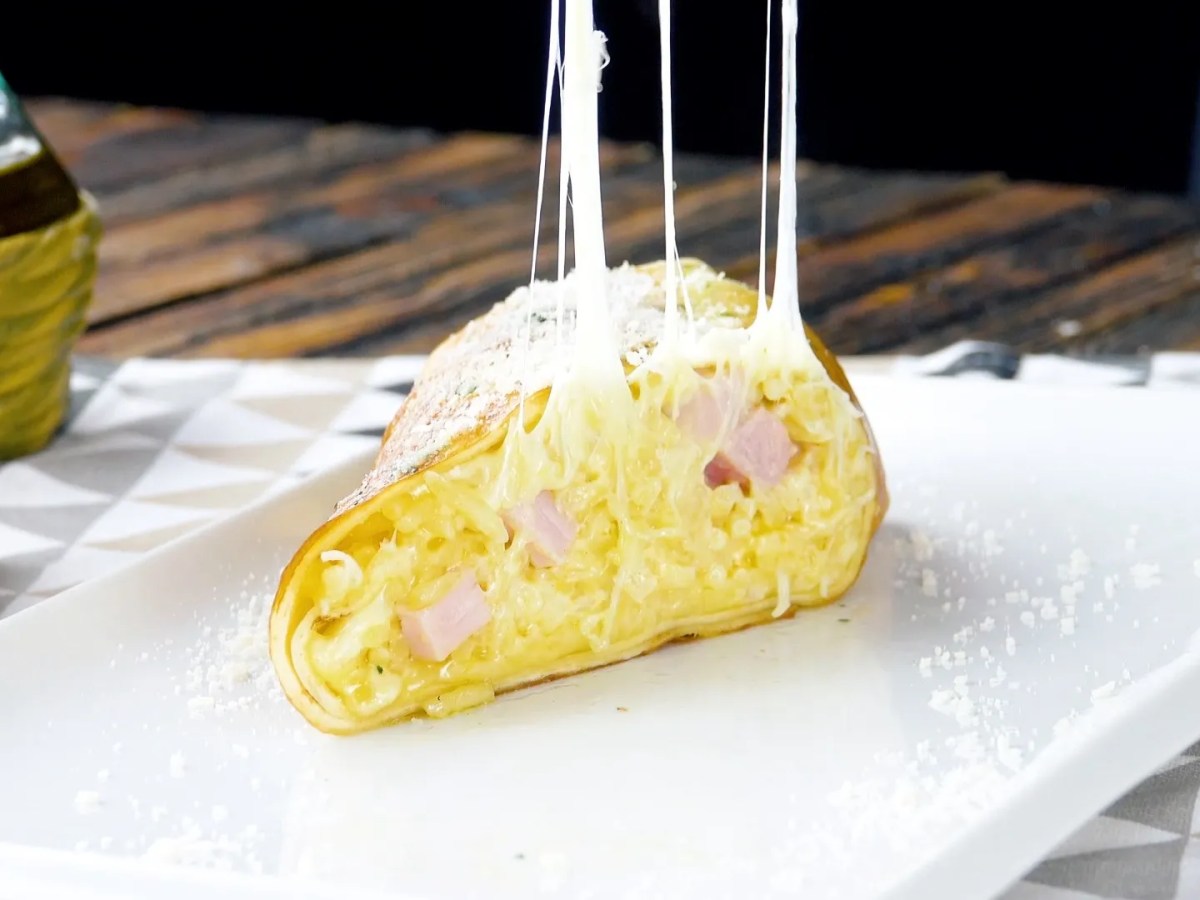Ein Carbonara-Nudel-Burrito auf einem Teller, aufgeschnitten.