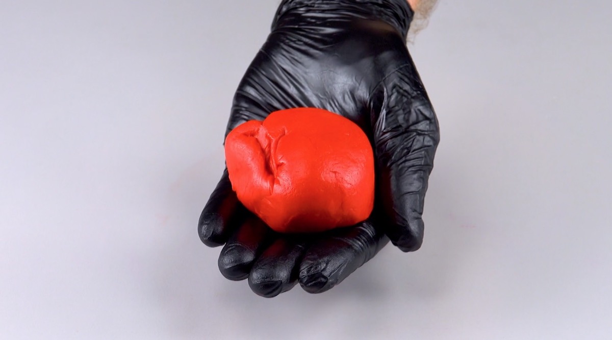 Roter Teig wird in Hand mit schwarzem Handschuh gehalten