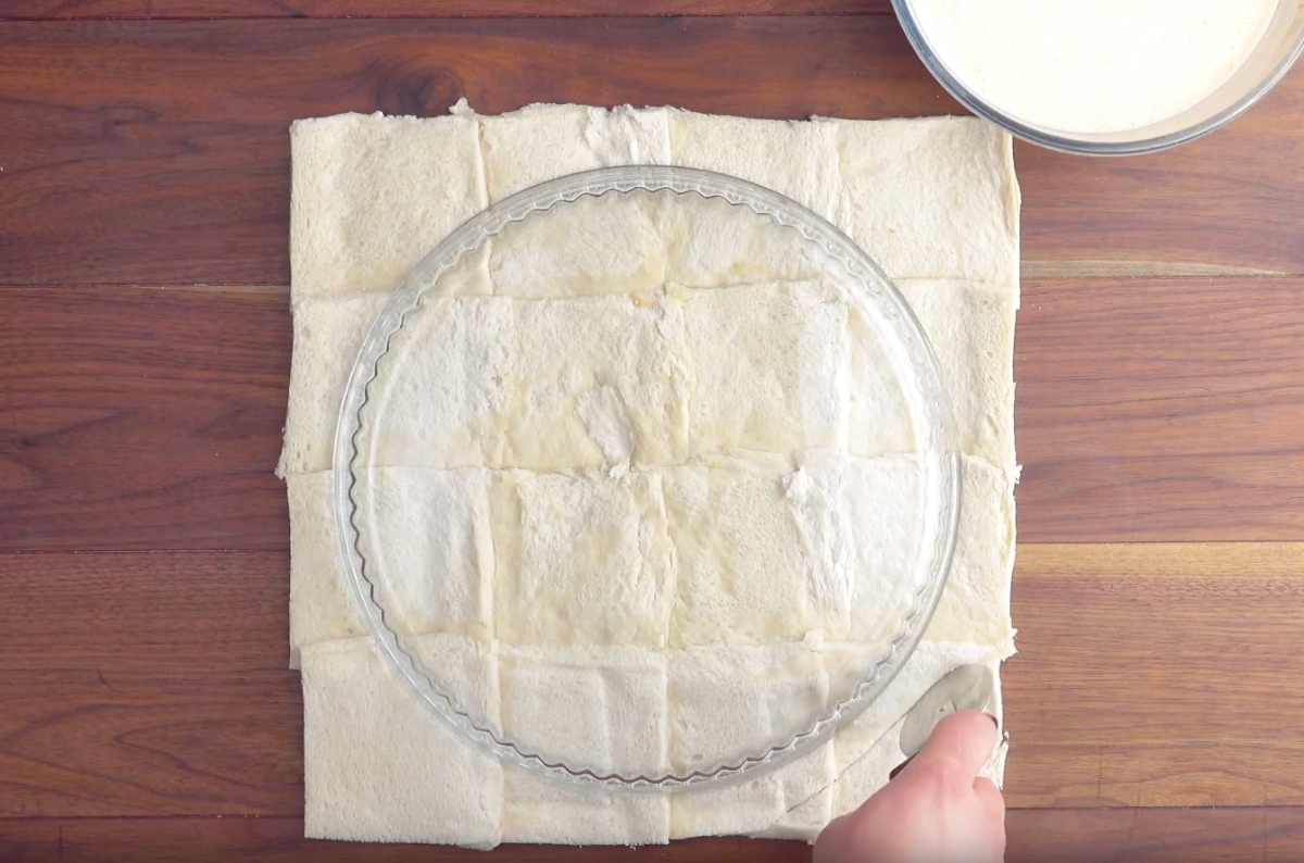Eine Tarteform liegt verkehrt herum auf Teig aus plattierten Toastscheiben.