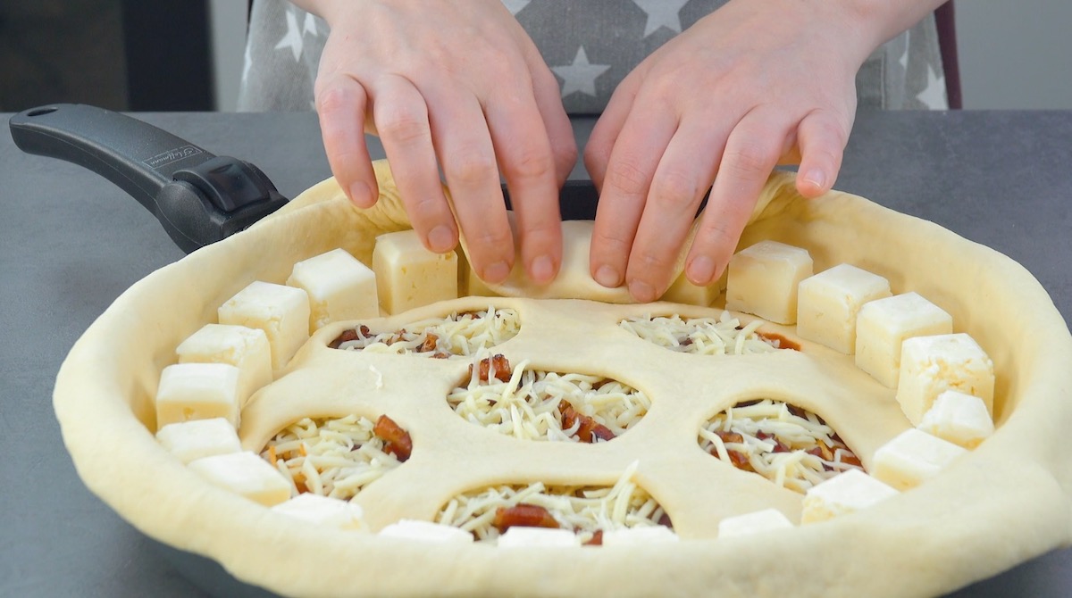 Pizzateig wird um MozzarellawÃ¼rfel geklappt, die am Rand von Pfannenpizza liegen