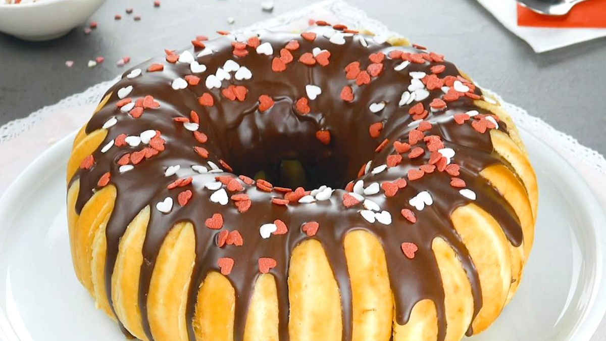 Donut-Kuchen aus 16 Teigkringeln, verziert mit Schokolade und bunten Streuseln. Serviert auf einem Teller.