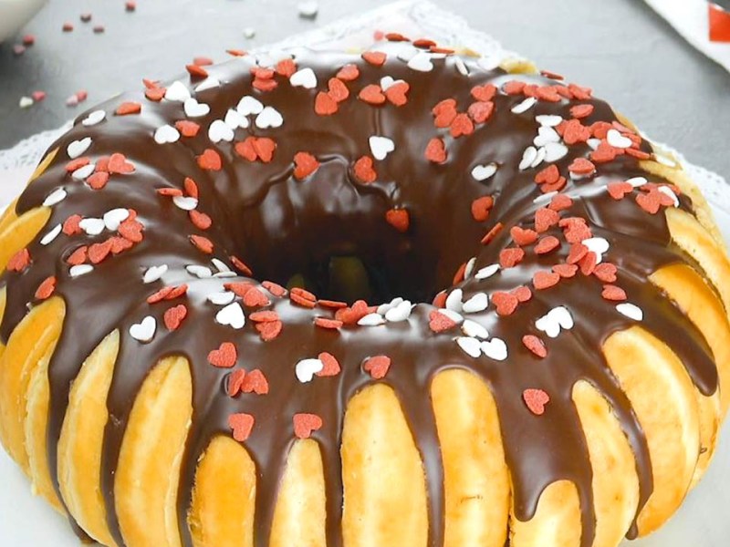 Donut-Kuchen aus 16 Teigkringeln, verziert mit Schokolade und bunten Streuseln. Serviert auf einem Teller.