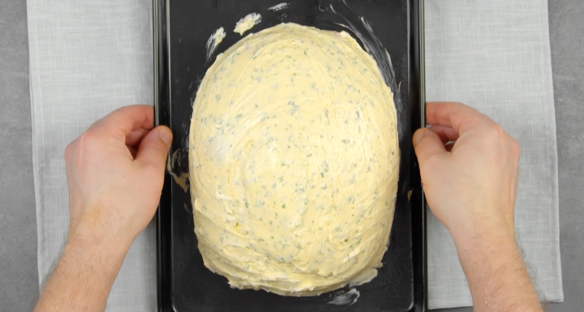 Kräuterbutter wird über gesamtem Hähnchen verteilt, das auf Backblech liegt