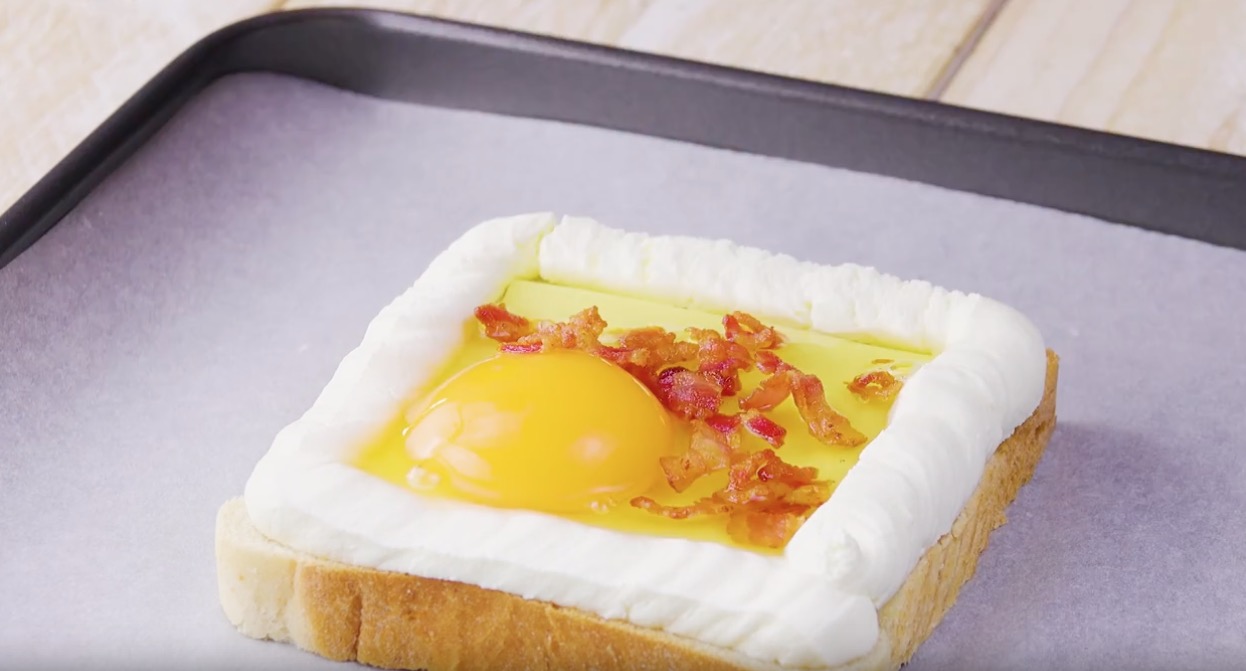 Toastscheibe auf Backblech wird mit FrischkÃ¤se am Rand und BaconsÃ¼ckchen und Ei in der Mitte belegt 