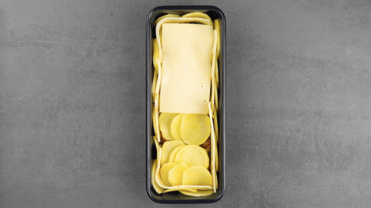 Hackfleisch in der Kastenform wird mit Kartoffelscheiben und Käse bedeckt