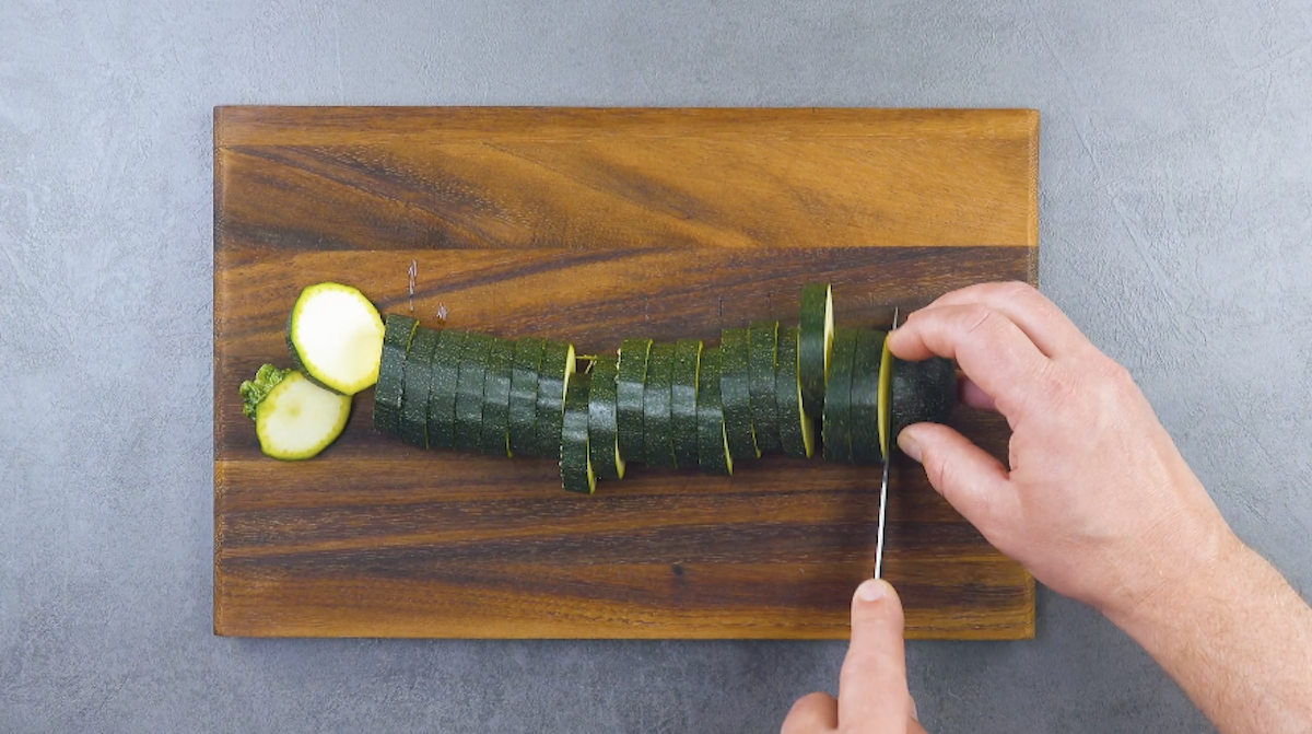 Eine Zucchini wird auf einem Holzbrett in Scheiben geshcnitten