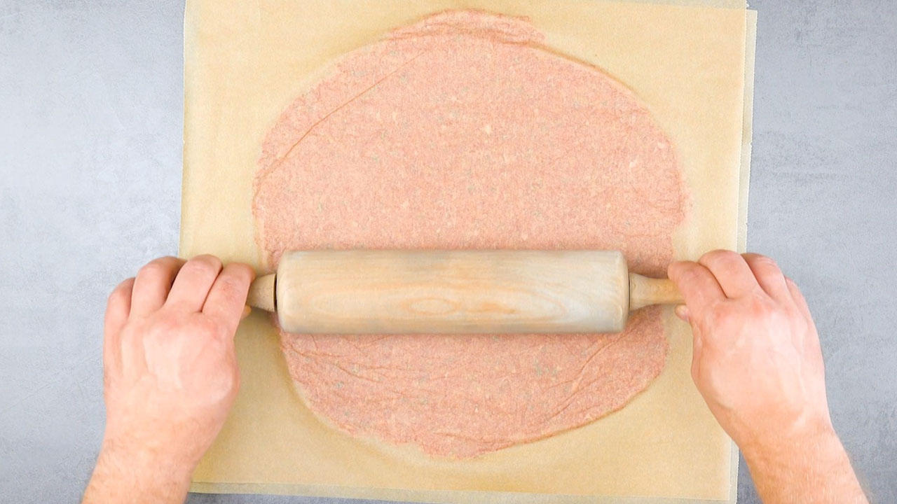 Hackfleisch wird zwischen zwei Backpapierstreifen gelegt und mit Nudelholz platt gewalzt