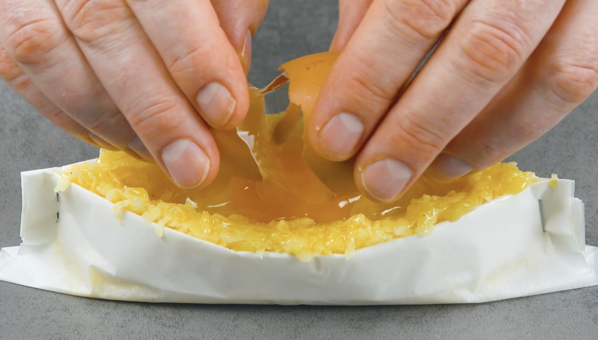 Ein Ei wird in Kartoffelmasse in Backpapierbooten aufgeschlagen
