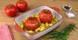 2 Tomaten mit Risotto-Füllung in der Auflaufform. Daneben 2 weitere Tomaten, eine Serviette, ein Bund Rosmarin und Schalen mit Pfeffer und Salz.