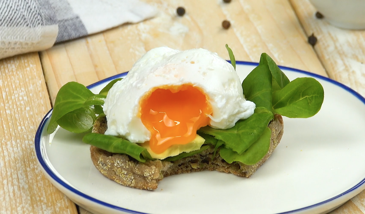 Pochiertes Ei auf dunklem Brötchen und Salat