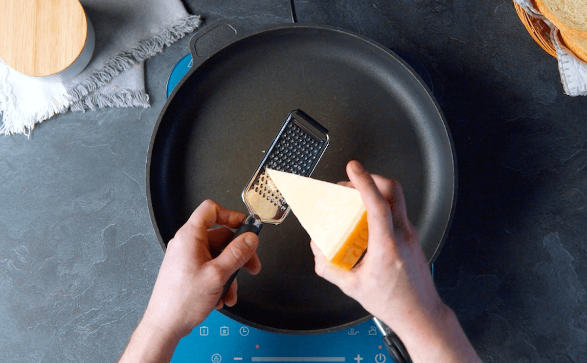 Parmesan wird in eine Pfanne gerieben