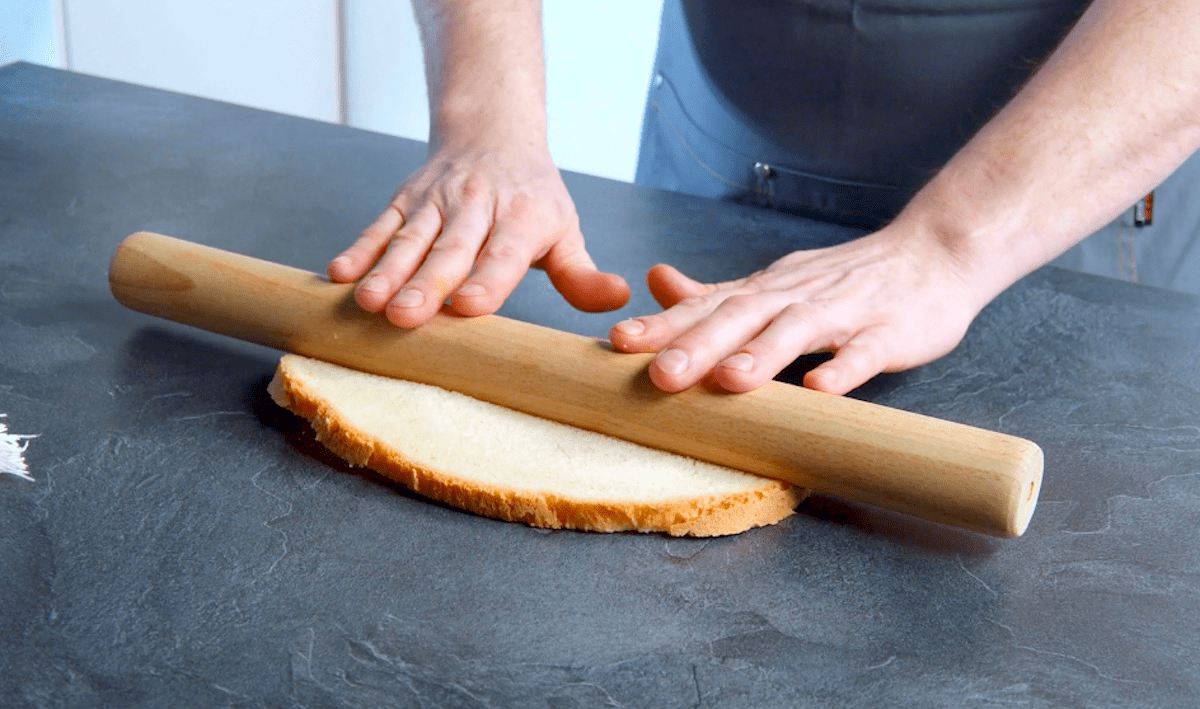 Eine ovale Scheibe Weißbrot wird mit einem Nudelholz plattgerollt