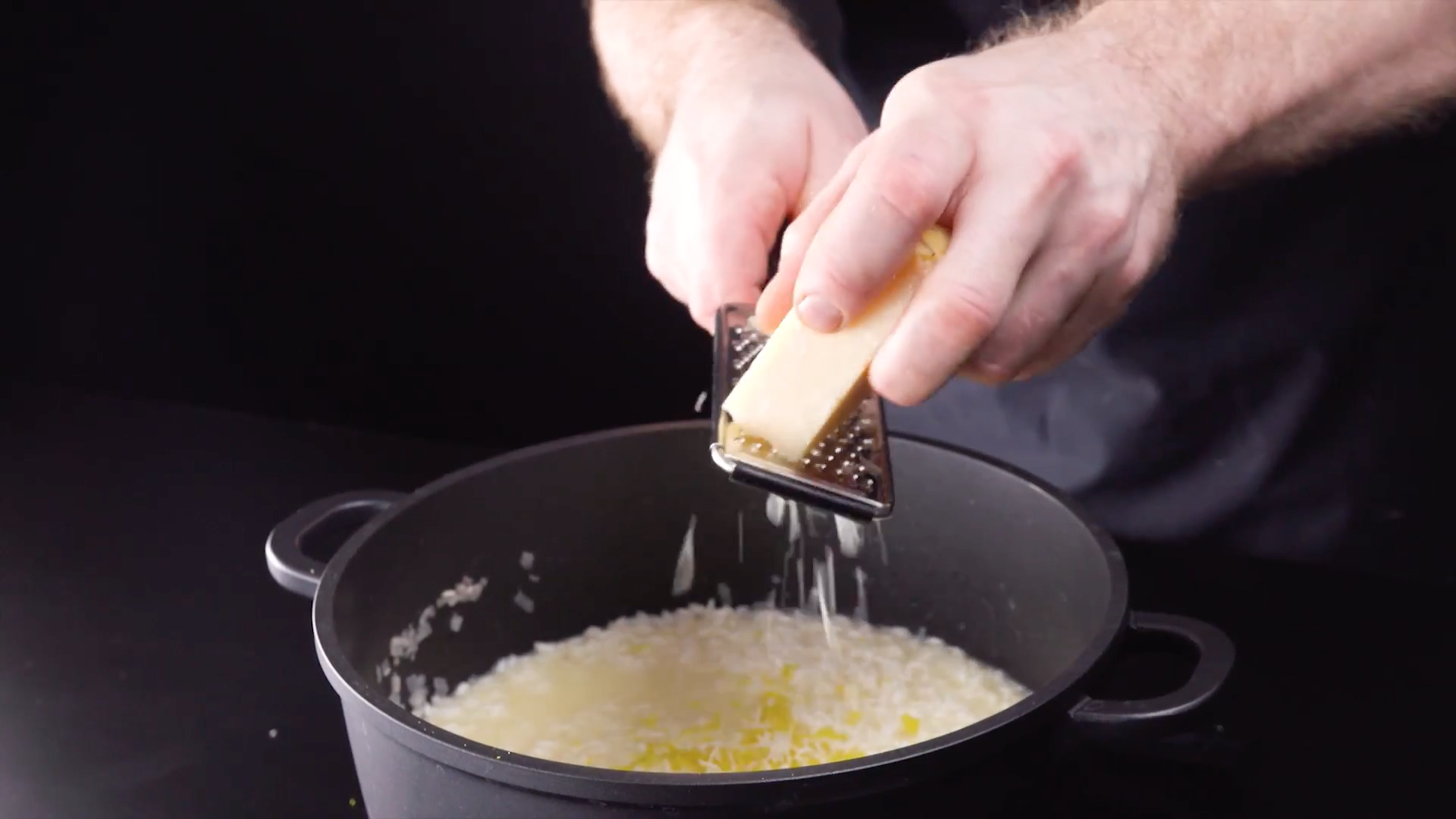 Parmesan wird zu Reis in einem Topf gerieben