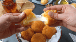 Ein Kartoffel-Käse-Bällchen über weiteren Bällchen auf einem Teller wird mit zwei Händen auseinander gezogen