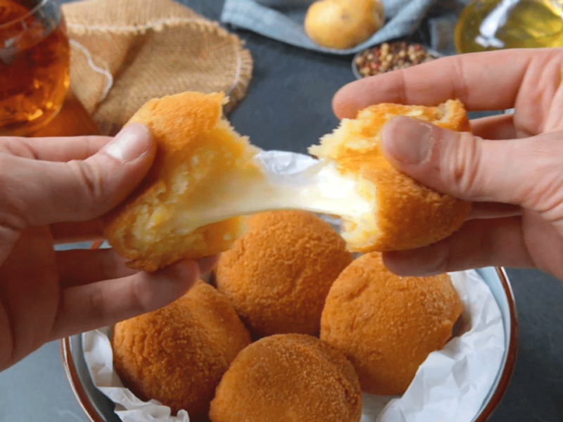 Ein Kartoffel-Käse-Bällchen über weiteren Bällchen auf einem Teller wird mit zwei Händen auseinander gezogen