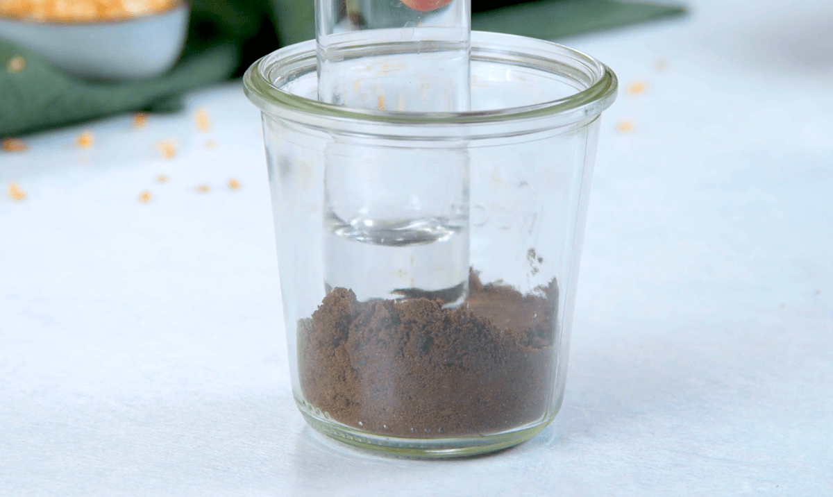 Zerbröselte Oreo-Kekse in einem Glas werden mit einem kleineren Glas auf den Glasboden gedrückt.