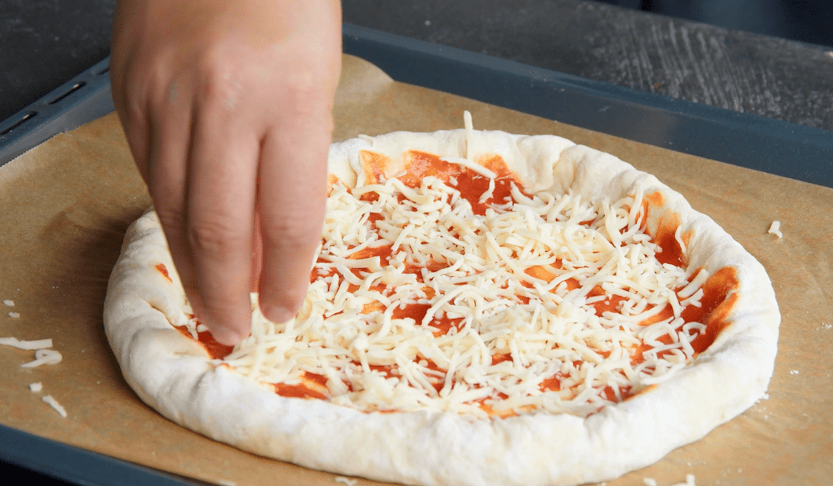 Pizzateig wird mit Tomatensauce und geriebenen KÃ¤se belegt
