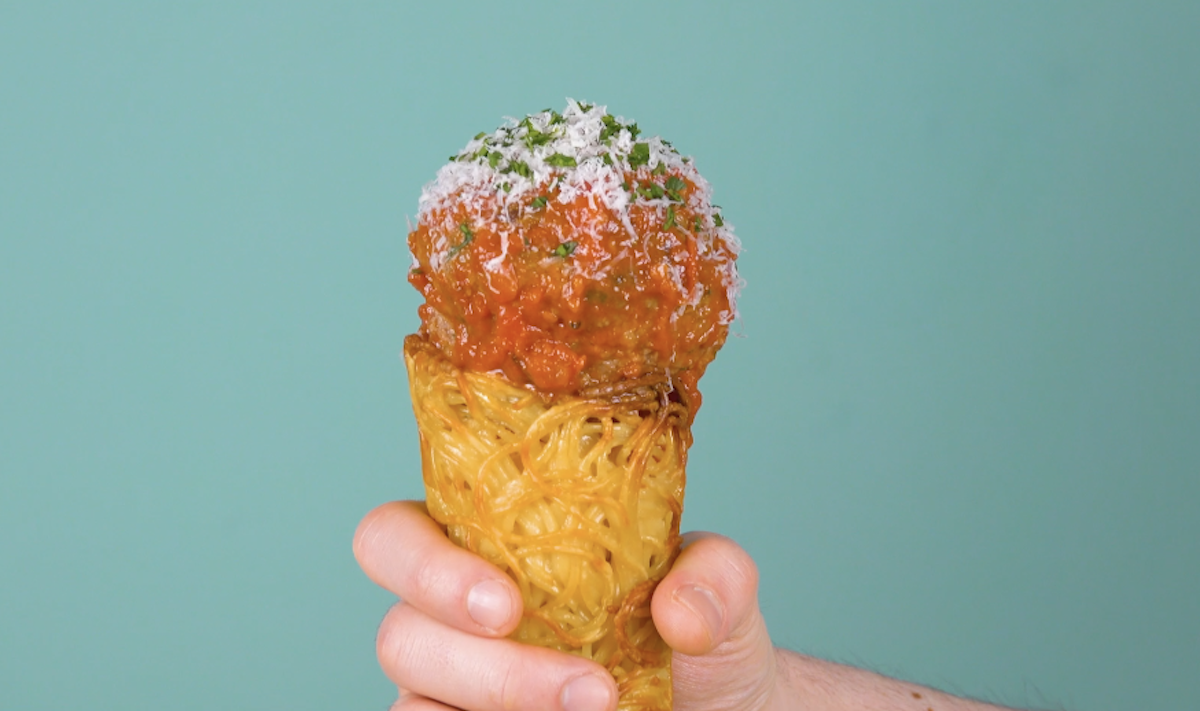 Spaghetti-Eis mit Hackfleischball wird in Hand gehalten