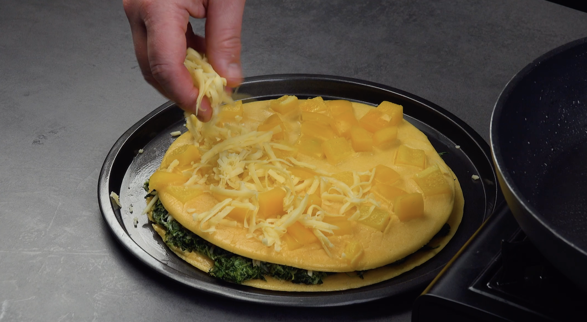 Auf die nÃ¤chste Schicht Omelett-Pfannkuchen werden kleingeschnittene gelbe Paprika und geriebener KÃ¤se gestreut