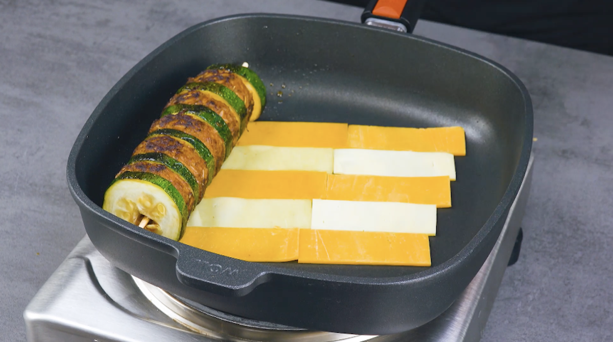 Pfanne wird mit unterschiedlich farbigen KÃ¤sestreifen ausgelegt und der Zucchini-Hackfleisch-SpieÃŸ am Ã¤uÃŸersten Rand platziert