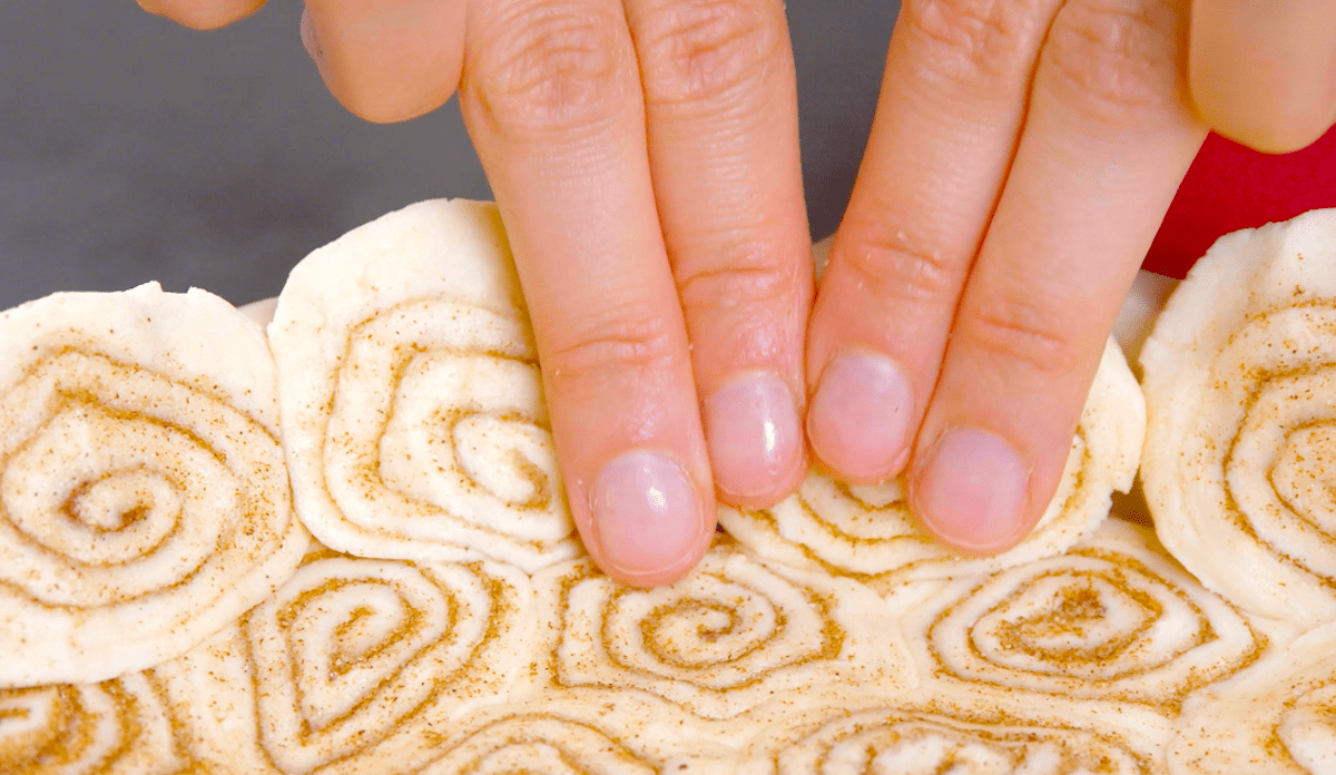 Zwei Hände drücken Zimtschnecken in eine Kuchenform