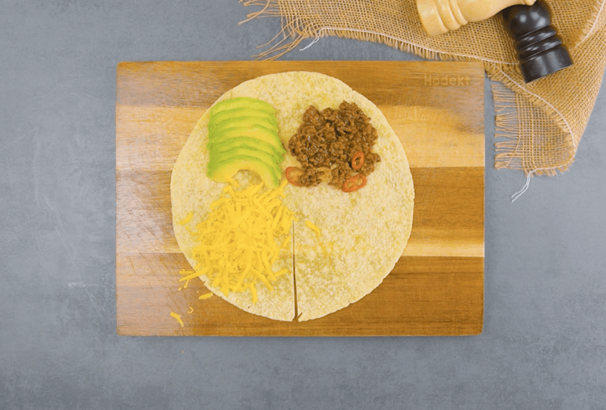 Ein Tortilla wird mit Avocado, Hackfleisch und Cheddar belegt