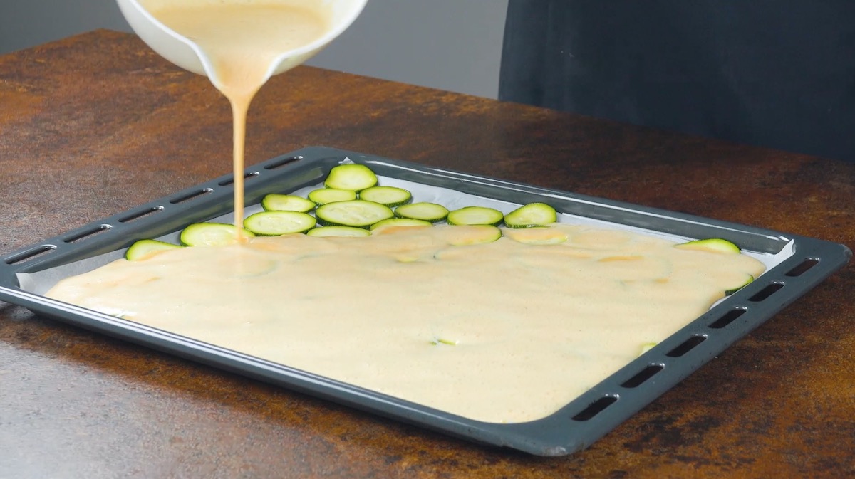 Verquirlte Eier werden über Zucchinischeiben auf Backblech gegossen