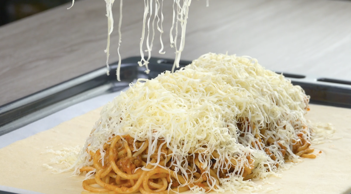 Spaghetti bolognese auf Pizzateig werden mit geriebenem KÃ¤se bedeckt