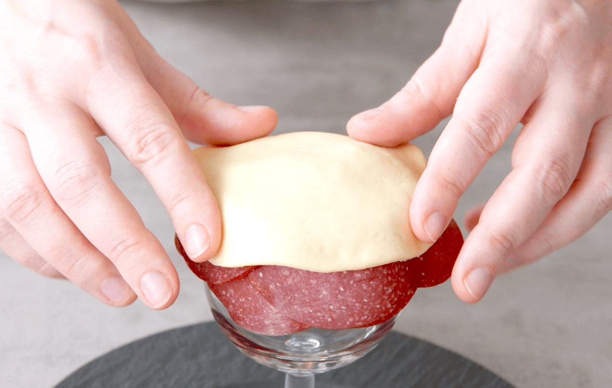 Pizzateig wird auf Salami gedrÃ¼ckt