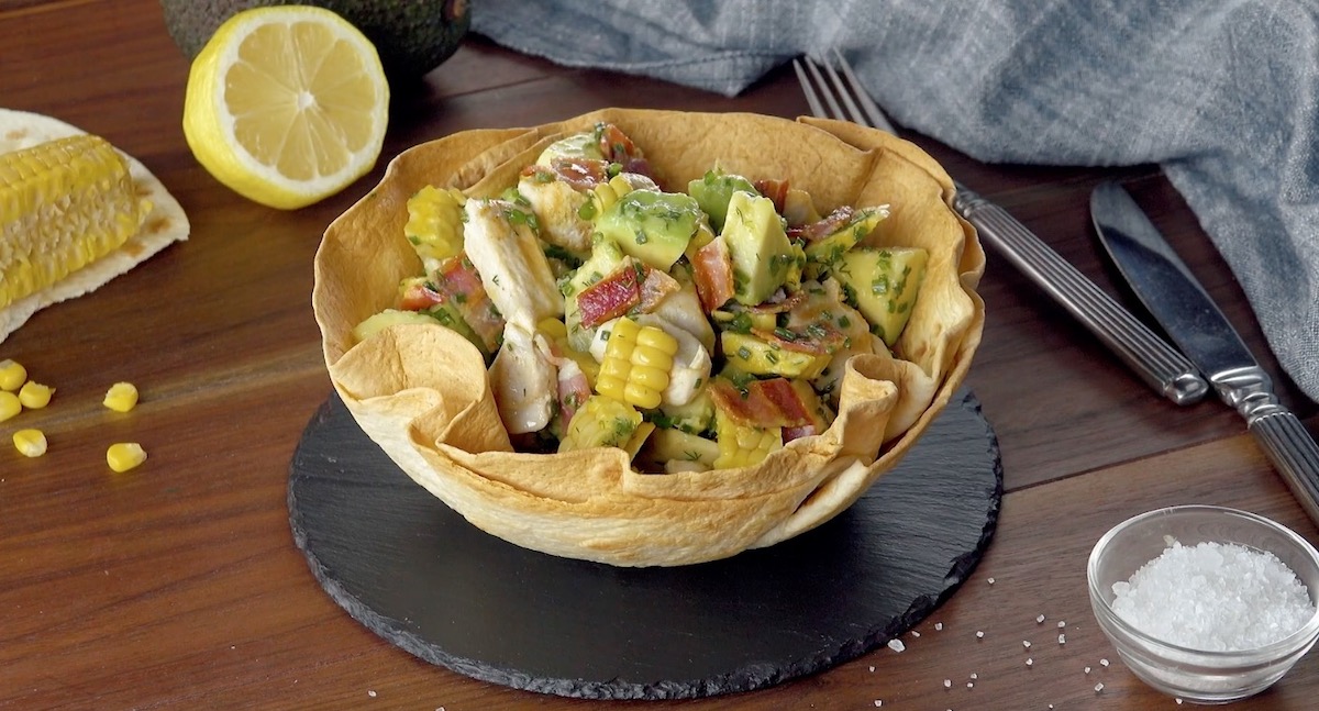 Avocado-Hähnchen-Salat in essbarer Tortillaschüssel auf einer Schieferplatte.