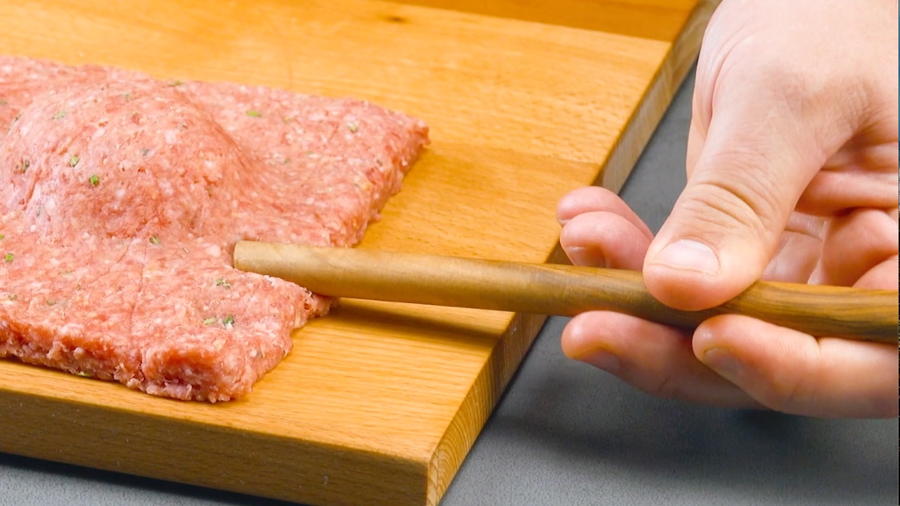 Die RÃ¤nder des Meatioli werden mit dem Griff eines HolzlÃ¶ffels eingedrÃ¼ckt