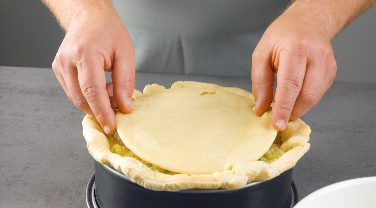 Ein Kreis aus Pizzateig wird in eine Springform als Decke gelegt