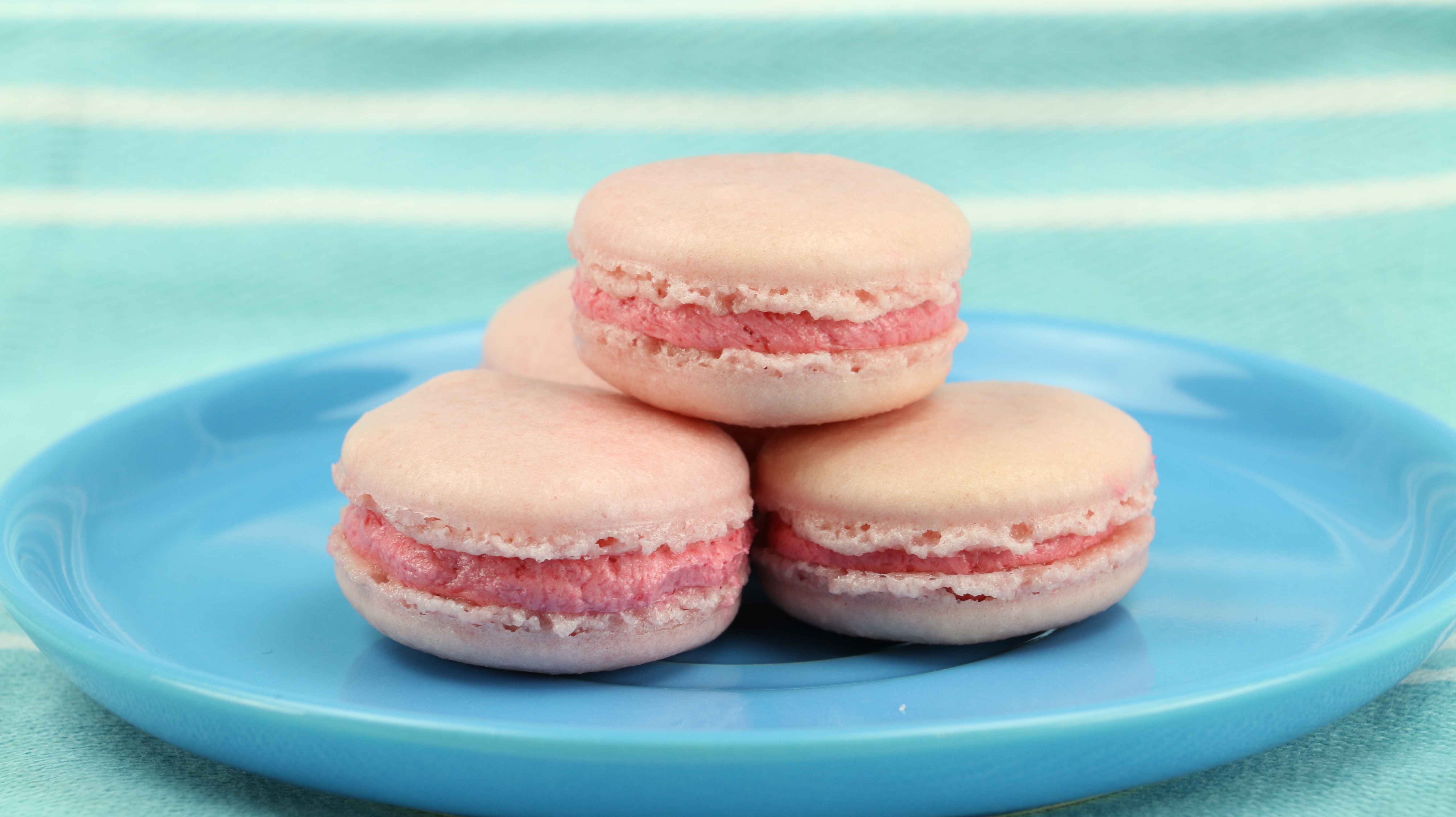 Vier rosafarbene Macarons auf einem Teller, die übereinander gestapelt wurden.