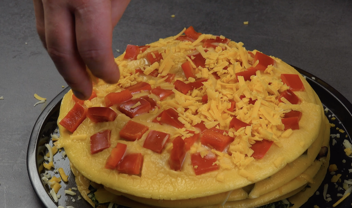Die vorletzte Schicht des Omelett-Kuchens wird mit rotem Paprika und geriebenem Cheddar bestreut