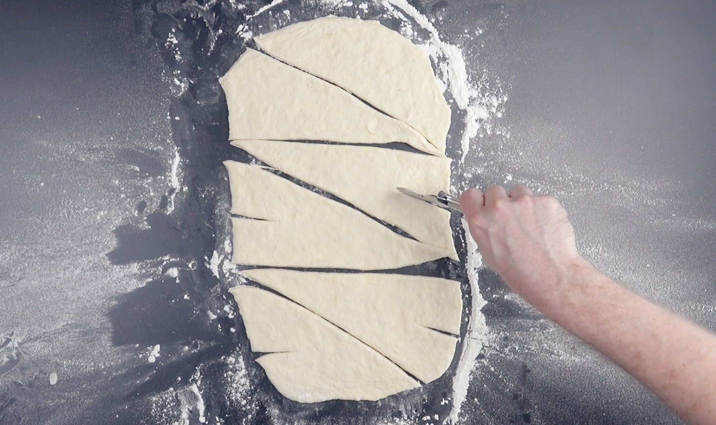 Gewalzter Croissant-Teig wird mit Pizzaschneider in spitzwinklige Dreiecke geschnitten