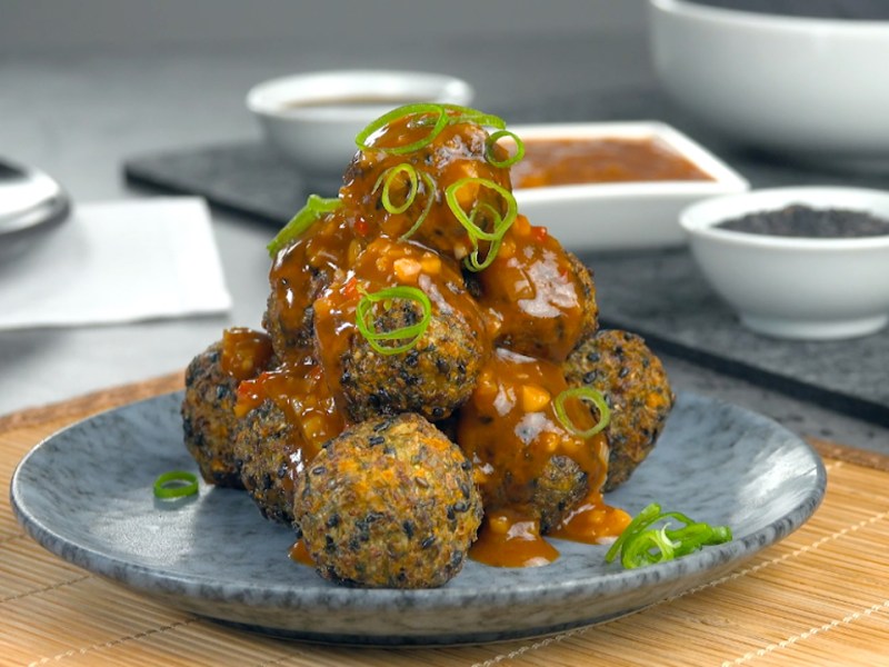 Eine Pyramide aus frittierten Gemüsebällchen mit Spitzkohl und schwarzen Sesamauf einem Teller.