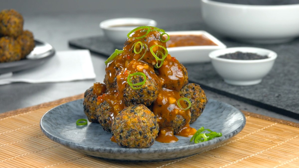 Eine Pyramide aus frittierten Gemüsebällchen mit Spitzkohl und schwarzen Sesamauf einem Teller.