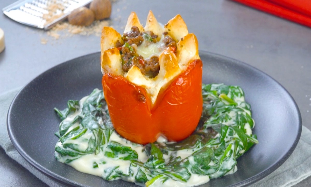 Eine gefüllte Paprika mit Hackfleisch auf einem Teller, die aussieht wie eine Blume. Dazu gibt es Spinat-Sahne-Soße.