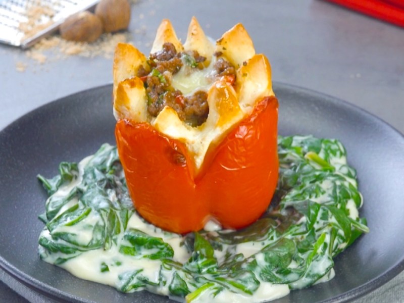 Eine gefüllte Paprika mit Hackfleisch auf einem Teller, die aussieht wie eine Blume. Dazu gibt es Spinat-Sahne-Soße.