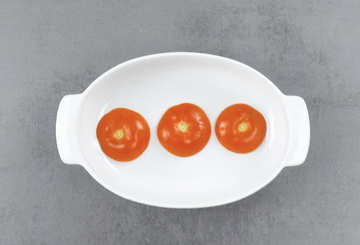 3 Deckel von Tomaten werden mit Strunk noch oben in ovale Auflaufform gelegt